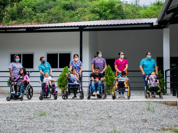 Six teachers standing behind six children in wheelchairs outside the preschool on its dedication day