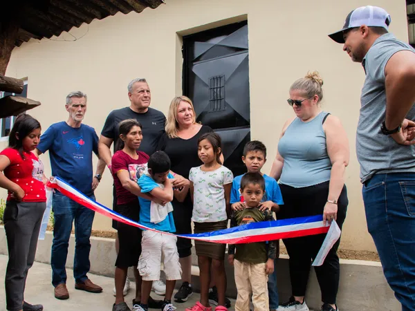 Darwin’s family and the Ryan’s Rays team cutting a red, white and blue ribbon at the front door of the new home