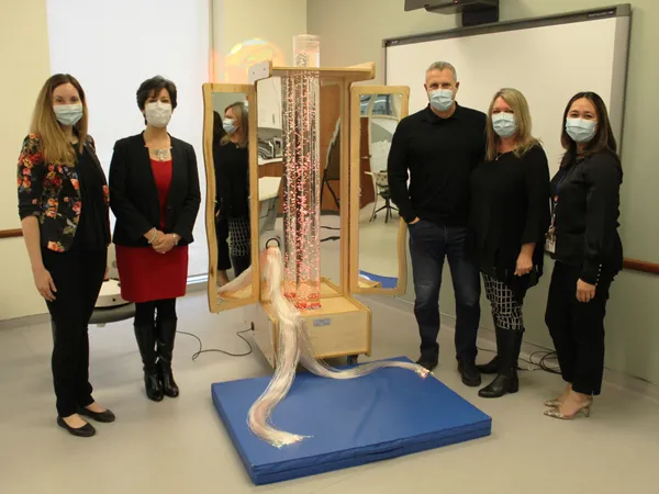 Five people in masks standing either side of a new Snoezelen cart with a lit bubble tube and fibre-optic strands in a hospital therapy room