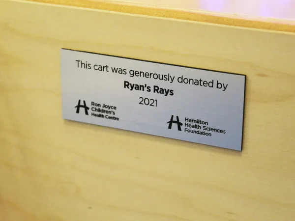 A plaque reading “This cart was generously donated by Ryan’s Rays 2021” with the Ron Joyce Children’s Health Centre and Hamilton Health Sciences Foundation logos