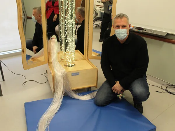 A man kneeling beside a Snoezelen cart, its fibre-optic strands spilling onto a blue mat