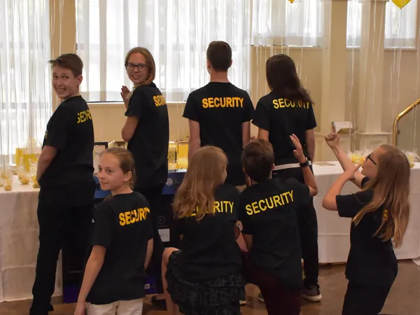 Young volunteers in black SECURITY T-shirts at a table beneath yellow balloons