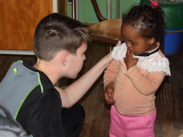 A teenage boy crouching down to greet a small girl in a classroom