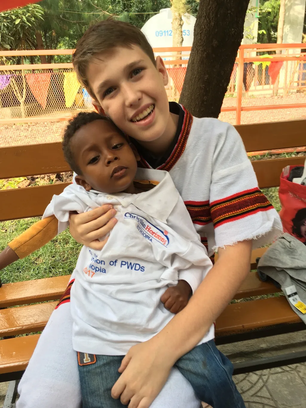 Devon, Ryan’s brother, holding a young boy named Dagim on his lap on a park bench in Ethiopia