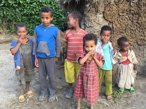 Six young children standing together in front of a mud-walled building