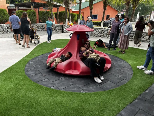 A man and children riding the red spinner in the playground while families look on