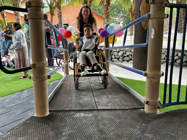 A woman pushing a boy in a wheelchair down the playground’s accessible ramp