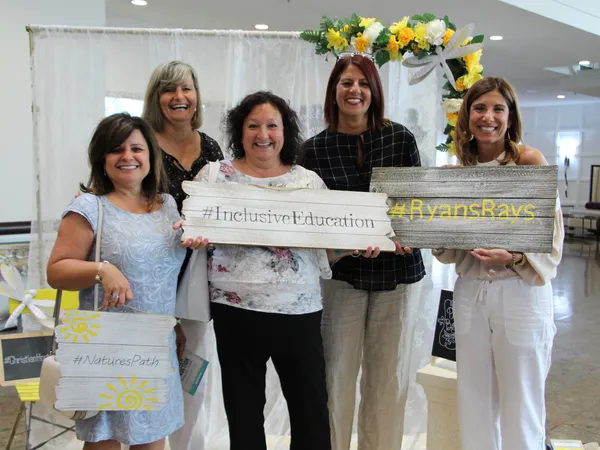 Five women holding painted wooden signs reading #InclusiveEducation and #RyansRays