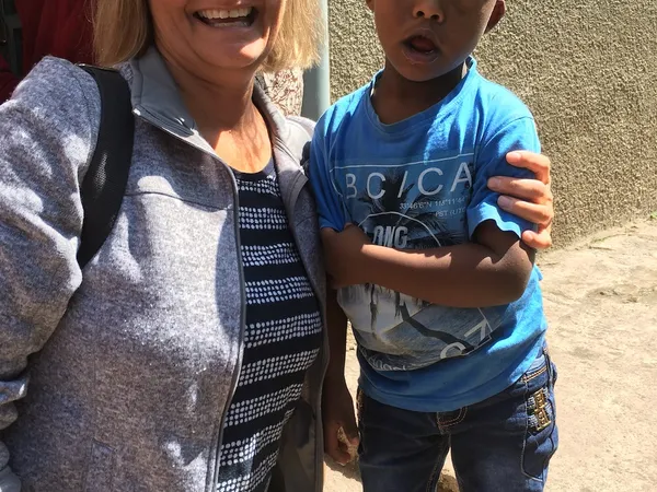 A woman with her arm around a smiling boy in a blue T-shirt outside a school