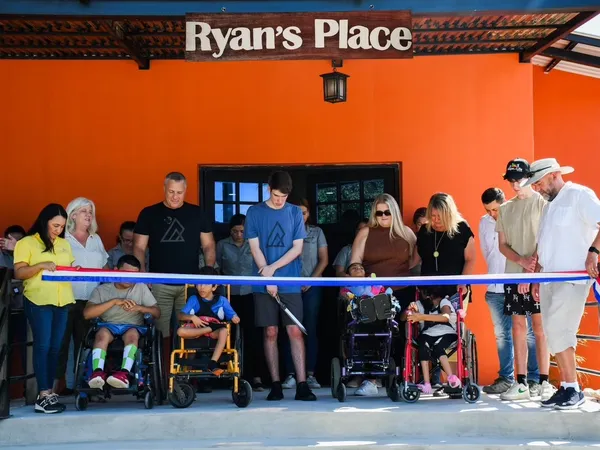 A ribbon being cut beneath the Ryan’s Place sign, with children in wheelchairs at the front of the crowd